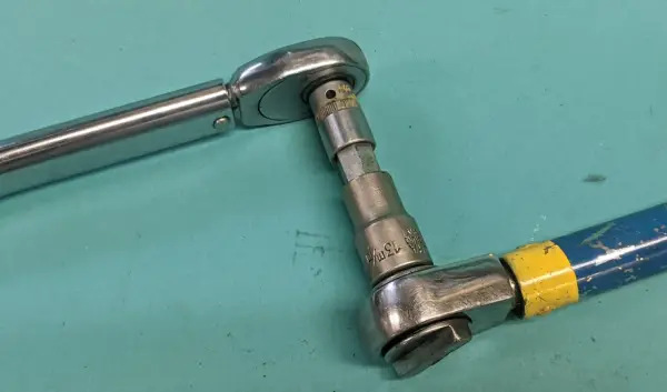 Två verktyg kopplade för att kalibrera momentnyckel. En momentnyckel i metall och en blå/gul skruvdragare med hylsa.
