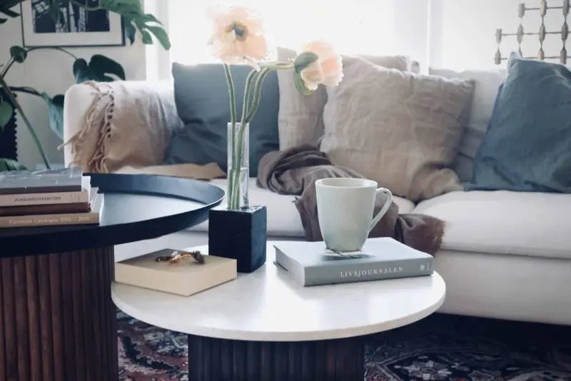 Ett stilrent soffbord med ribbad bas, perfekt för ditt hem. Här finns en bok, en mugg och en vas med blommor.